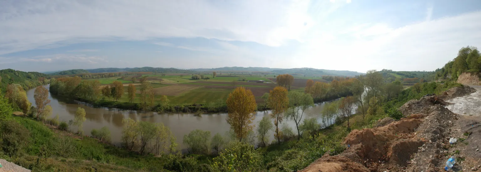Un large fleuve dessinant un long méandre paisible à travers des champs plats et verdoyants sous un ciel pâle