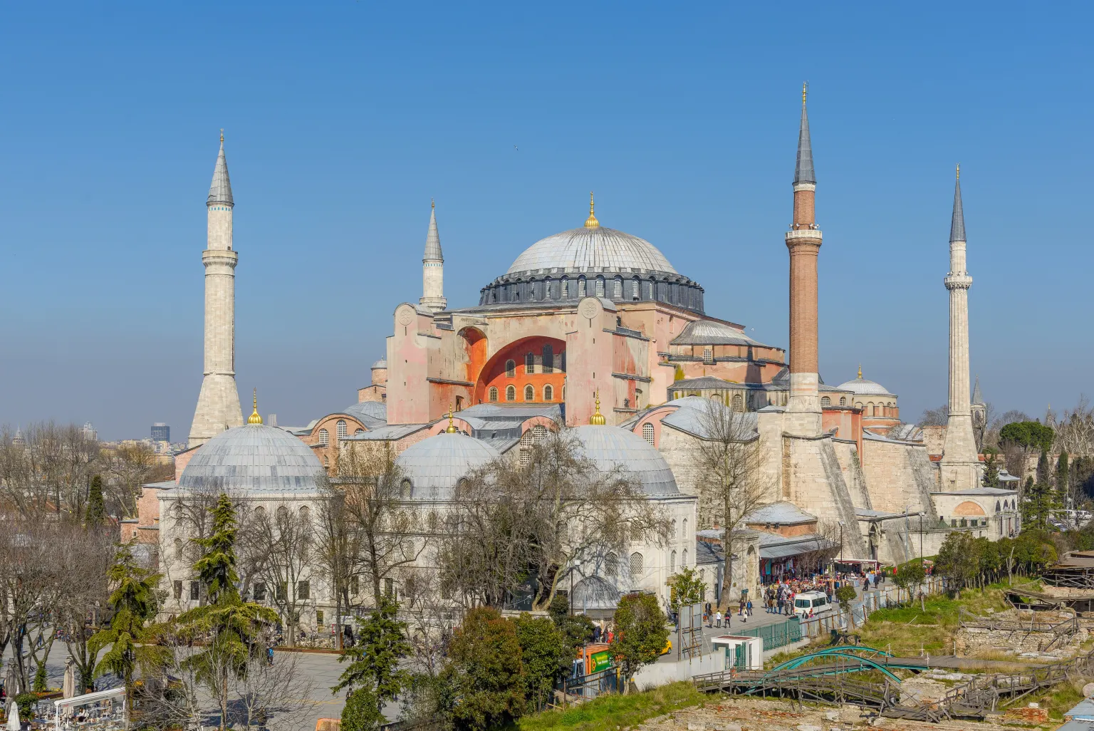 Santa Sofia com sua grande cúpula central e quatro minaretes, fotografada de um ponto elevado em um dia de céu limpo, com árvores sem folhas à frente